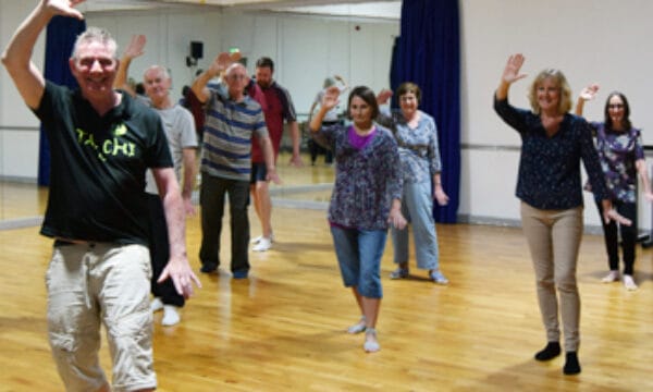 A group of people doing a tai chi pose, they are all smiling.