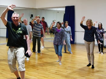 A group of people doing a tai chi pose, they are all smiling.