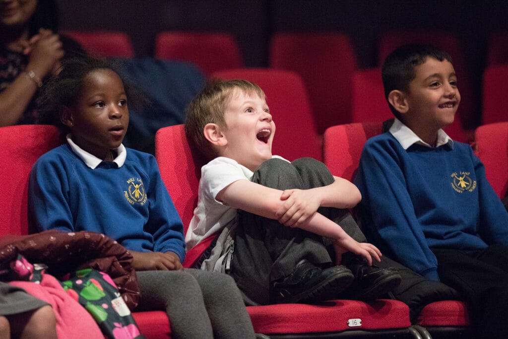 Three children seat in theatre seats enjoying a performance