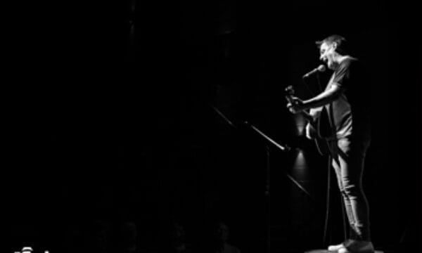 Black and white of a man standing on stage with a viold