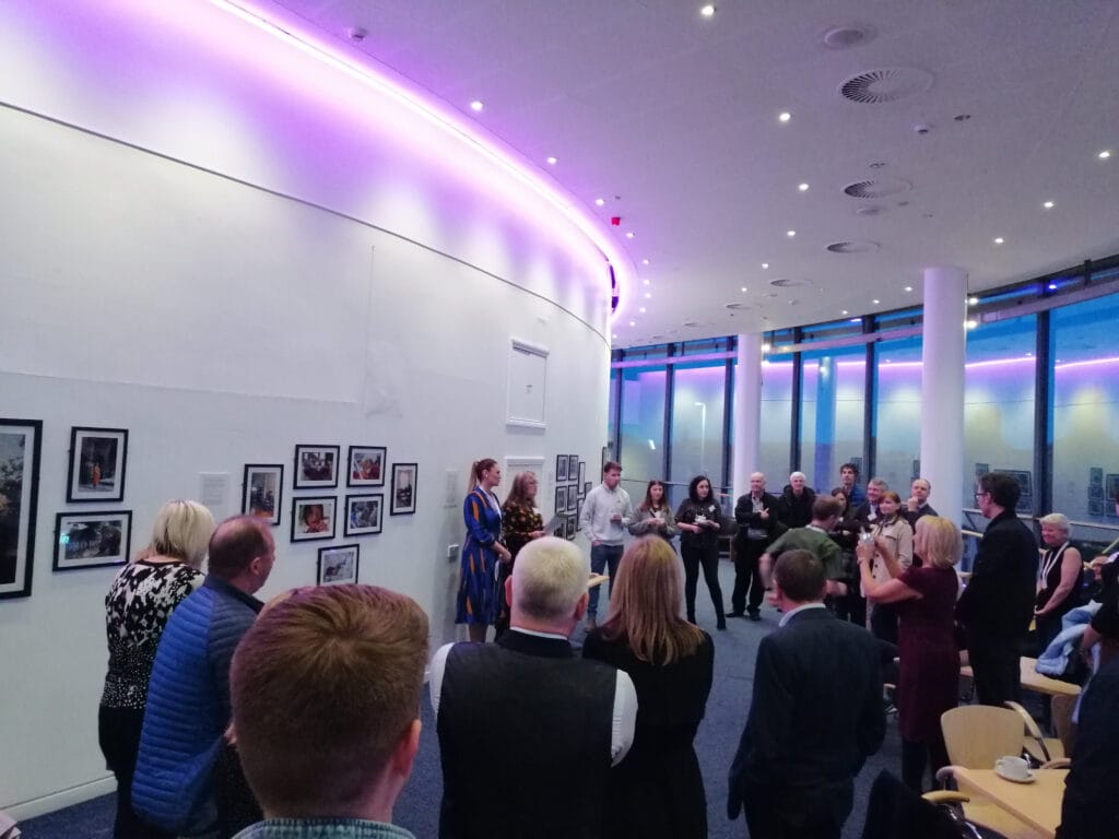 A crowd of people gathered in a gallery to view artwork lining the walls