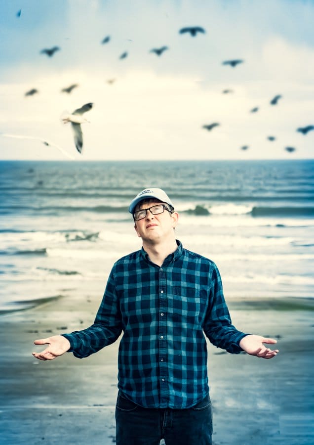 Mike Edwards standing a beach surrounded by seagulls