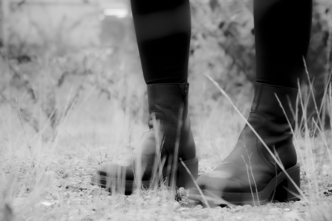 A black and white image of a person's lower legs and feet (wearing black boots).