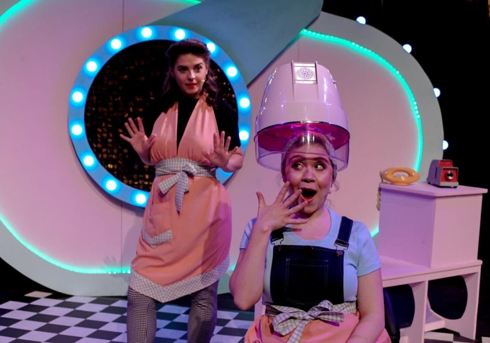 Two characters from Not So Ugly Sisters, one under a hairdryer