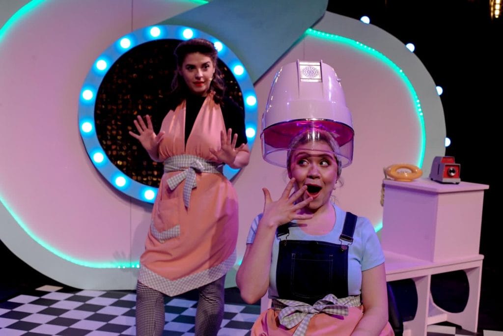 Two characters from Not So Ugly Sisters, one under a hairdryer