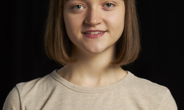 Headshot of Niamh Nelson. She is in her early 20s and has mid-brown straight haior that falls just under chin length. She is wearing a short-sleeve, beige coloured top.