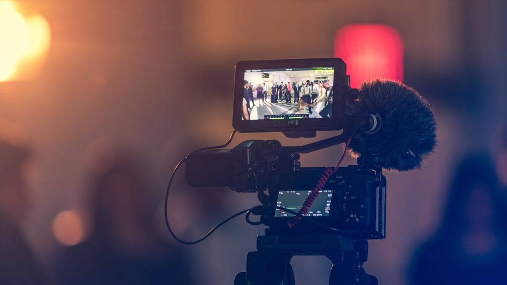 A video camera recording a group of people. The background is out of focus.