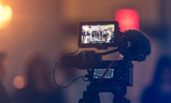 A video camera recording a group of people. The background is out of focus.