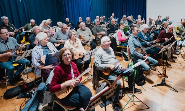 A room packed with people, they are all seated and playing ukuleles.