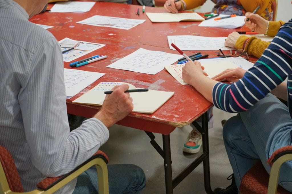 Two people working on hand-lettering, they are both holding colourful pens.