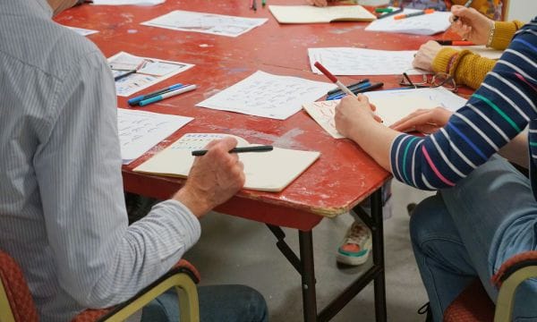 Two people working on hand-lettering, they are both holding colourful pens.