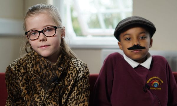 Two primary school children dressed up as themselves 50 years in the future. The boy is wearing a fake moustache.