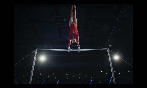 Actor playing Olga wearing a red leotard on gymnastic bars