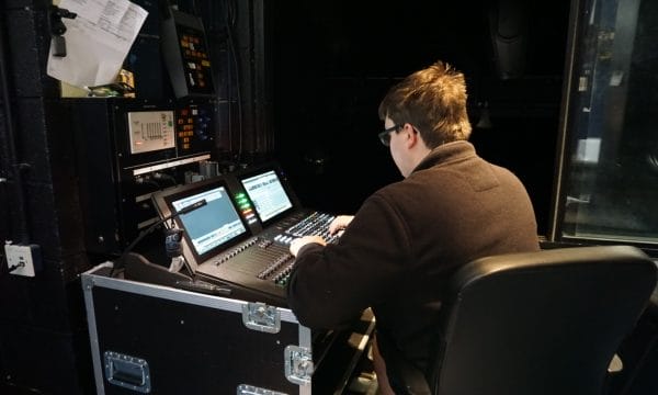 A technician sits operating a lighting/sound desk