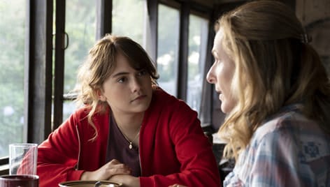 A young dark haired girl and an older blond woman sit having a conversation at a table