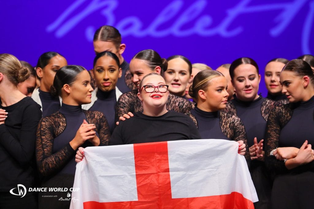 A group of dancers with one at the front holding an England flag