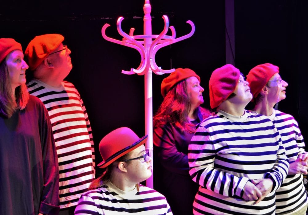 Six members of Full Circle Theatre Company gathered around a tall white hat stand