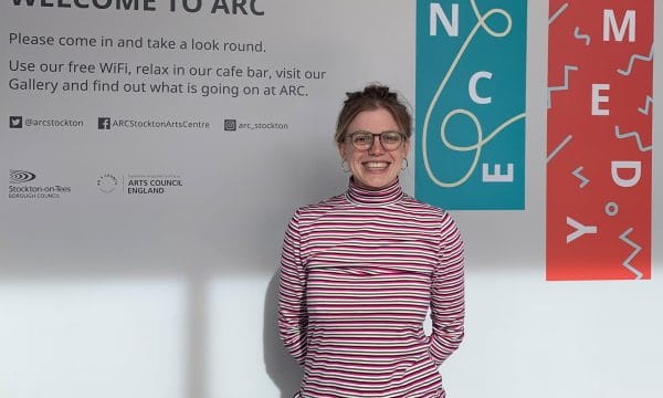 Cristina smiles for the camera in ARC's foyer, standing in front of the 'WELCOME TO ARC' sign