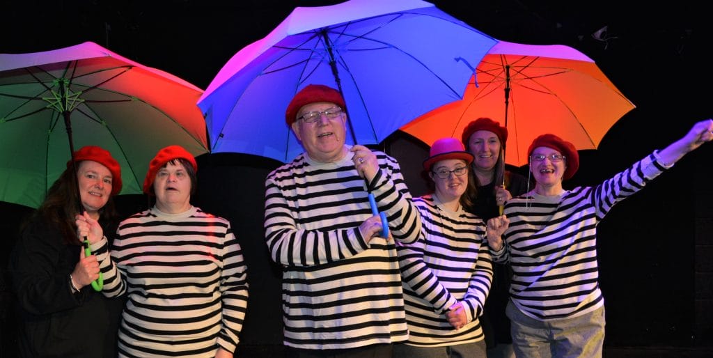 Performers from Full Circle, wearing matching striped tops, hold blue and red umbrellas