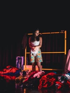 A cast member stands and looks at piles of coloured material around their feet