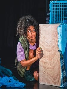 A cast member is crouching, and appears to be hiding behind a box with a worried look on their face