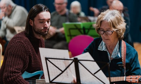 ARCulele tutor Stephen sits beside a participant, they are both looking at sheet music and Stephen is explaining how to read it.