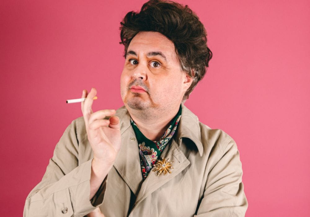 A bright pink background, with Tommy in drag, cigarette in hand.