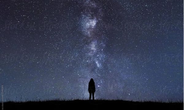 A small figure stands in silhouette against a star-filled night sky