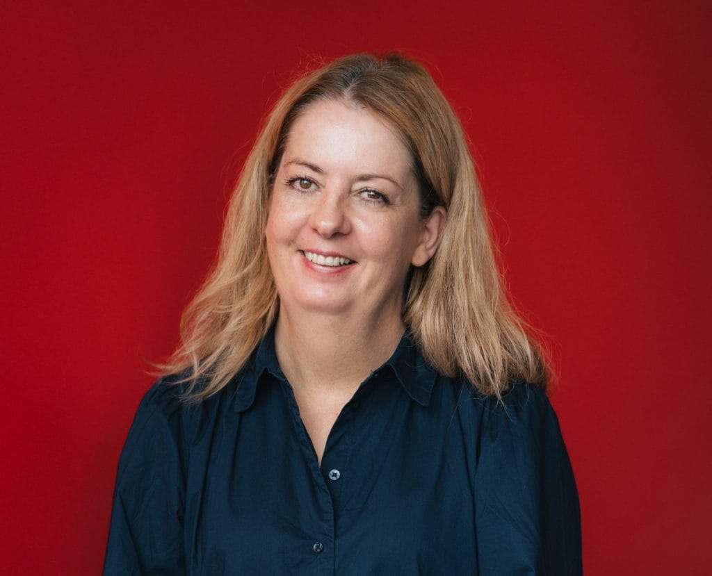 ARC's new Family Arts Coordinator Judith Crompton. Judith is a white woman with shoulder length blonde hair. She is wearing a long sleeved black blouse and smiling towards the camera.