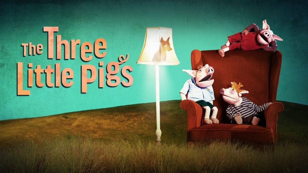 On the left hand side of the image is the show title, 'The Three Little Pigs'. On the right hand side are three puppet-style pigs, wearing clothes, sitting in various spots on the same large, red armchair. A standard lamp, switched on, is to the side of the chair. The shadow of a wolf is looking down at the pigs from inside the lampshade.