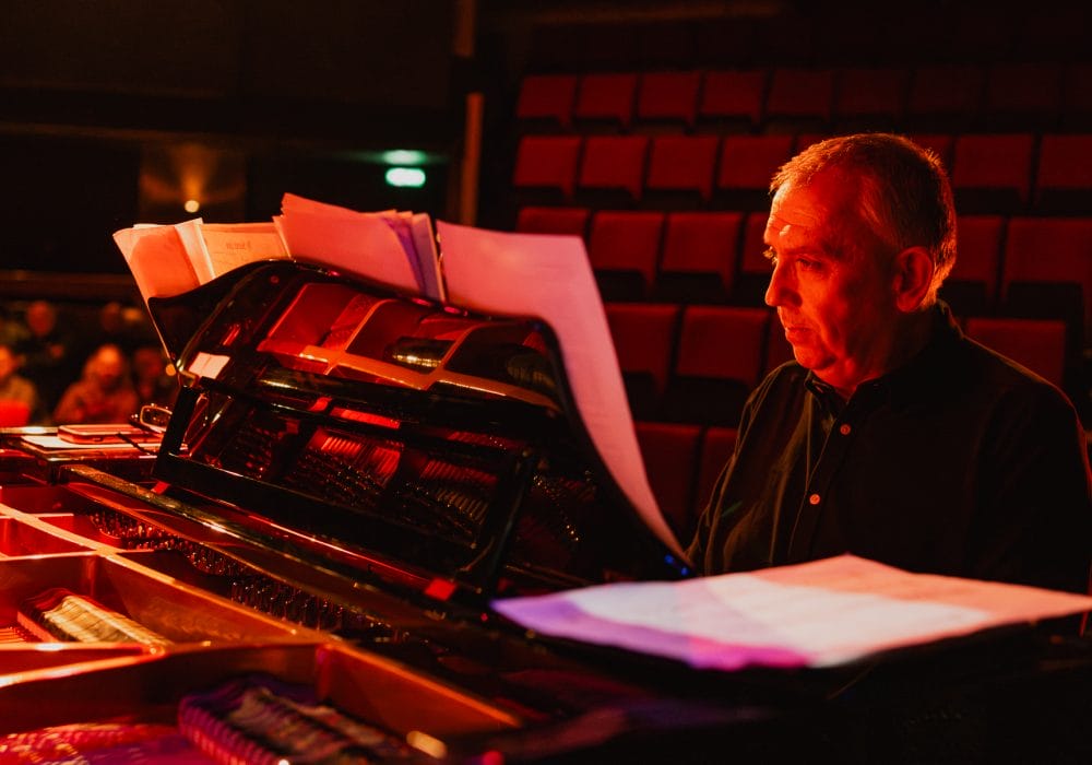 Jeremy sits at a piano on stage