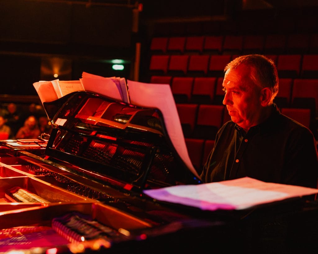 Jeremy sits at a piano on stage