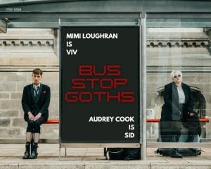 Two people in dark clothes sit at a bus stop on either side of a big advertising banner. The ad reads Mimi Loughran is Viv. Audrey Cook is Sid. Bus Stop Goths.