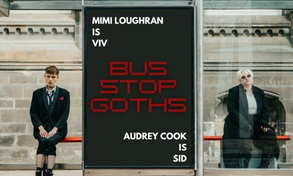 Two people in dark clothes sit at a bus stop on either side of a big advertising banner. The ad reads Mimi Loughran is Viv. Audrey Cook is Sid. Bus Stop Goths.