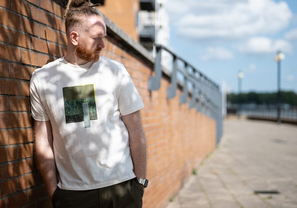 Newton Faulkner stands against a brick wall near what might be a pier