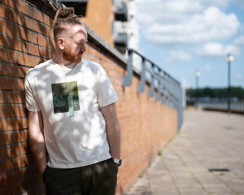 Newton Faulkner stands against a brick wall near what might be a pier