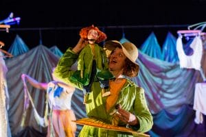 A performer with a puppet in an identical green outfit on her shoulder, in a production shot from The Selfish Giant. 