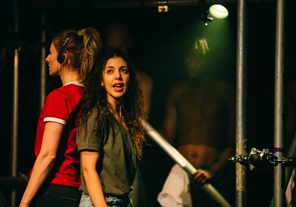 Two women, one wearing headphones, stand back to back