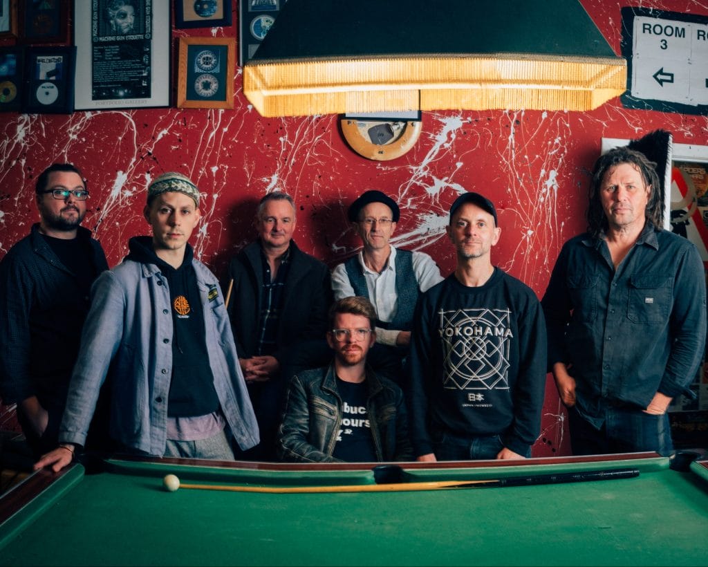 7 people from Peatbog Faeries stand against a snooker table