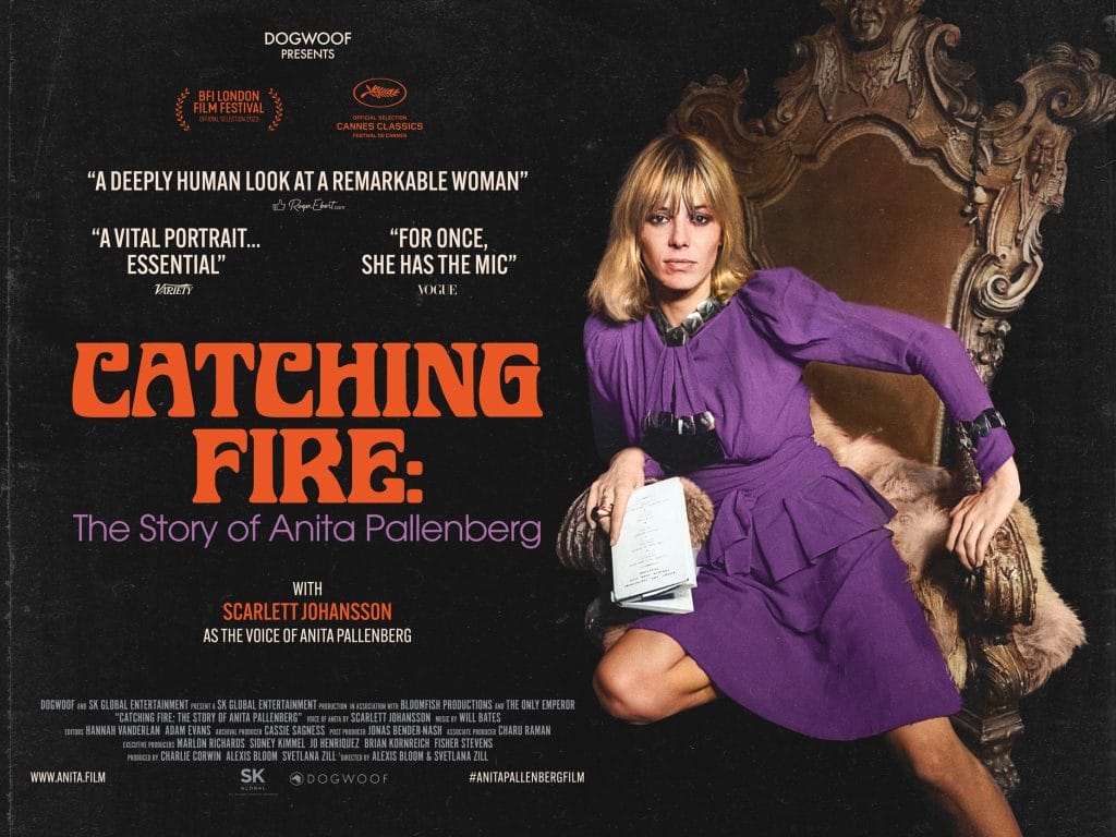 Catching Fire in Orange text with a white female with blonde hair in a long bob style with a fringe. She is wearing a long-sleeved purple long sleeved dress. She has one knee on an arm chair and one on the floor.