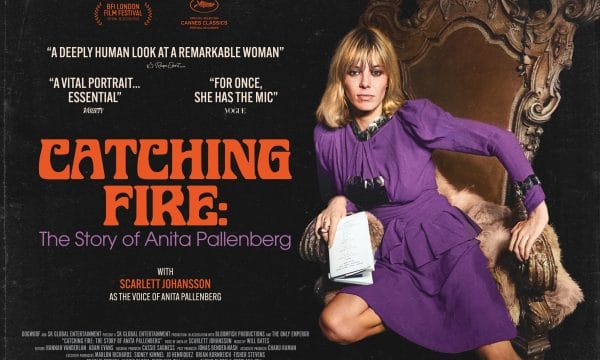 Catching Fire in Orange text with a white female with blonde hair in a long bob style with a fringe. She is wearing a long-sleeved purple long sleeved dress. She has one knee on an arm chair and one on the floor.