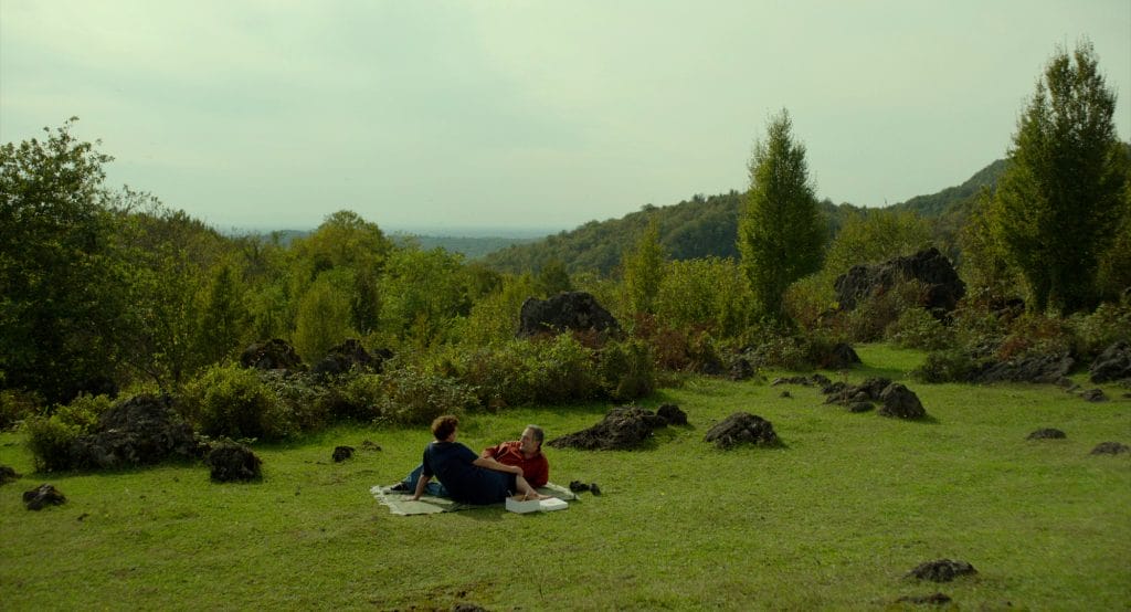 A beautiful large field with lots of green, featuring a couple relaxing whilst in conversation.