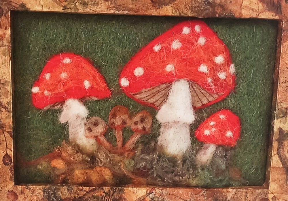 A framed needle felt painting of 3 red and white toadstools.