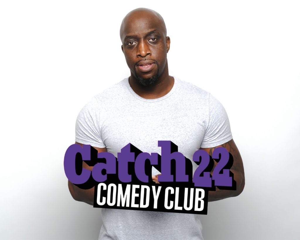 Black male with bald head wearing a white t-shirt. Catch 22 Comedy Club.