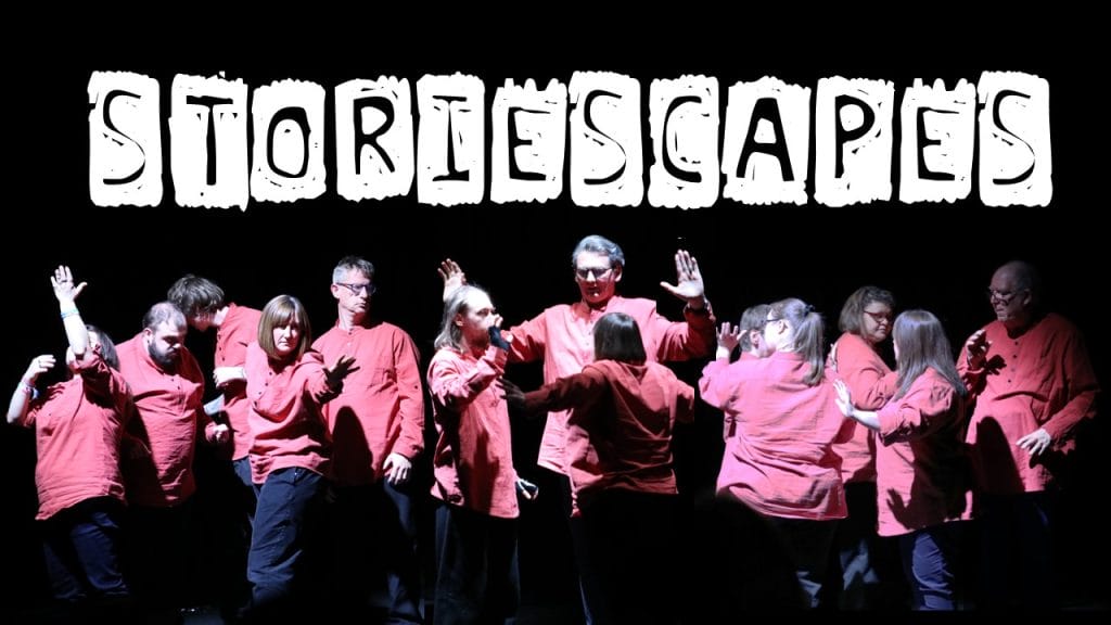 A group of performers in various poses, all wearing matching red shirts, against a plain black background. Text reading 'STORIESCAPES' is overlaid above their heads.