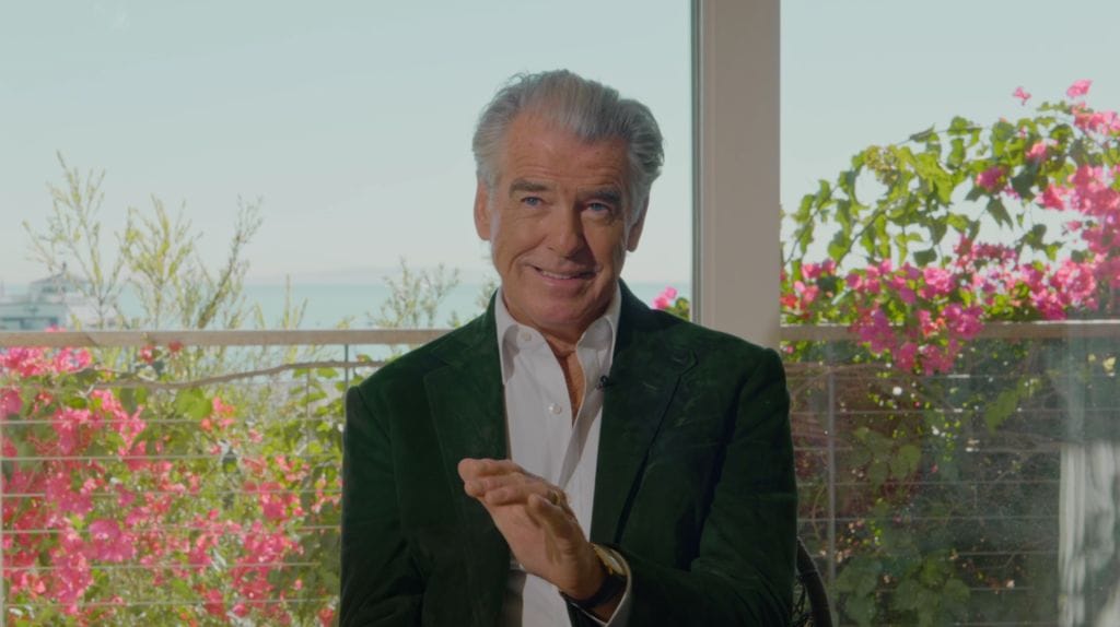 Headshot of Pierce Brosnan a white male with grey hair wearing a blue suit with white shirt.