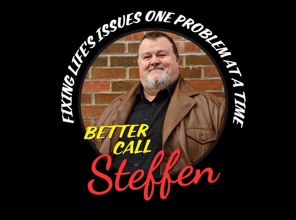 Black background with a circle image of a white male, short dark hair, grey beard, wearing a brown leather jacket and black shirt. He is stood against a brick wall.