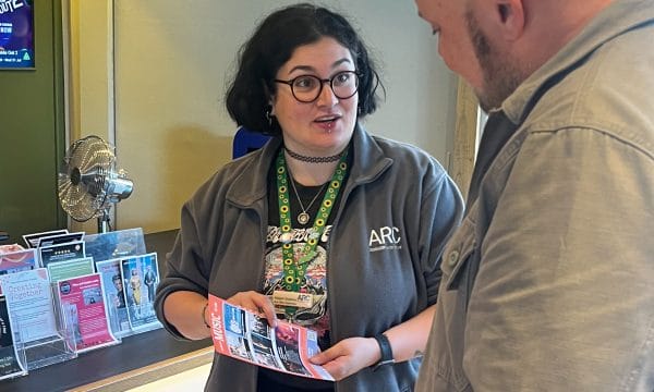 A person wearing an ARC branded jacket shows another person a flyer promoting some of ARC's shows