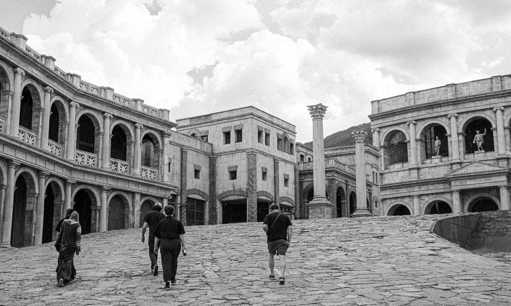 Black and white image of a group of five people walking up a paved bank towards some ancient buildings