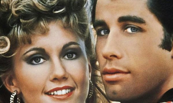 A close-up of Olivia Newton-John and John Travolta. Olivia Newton-John is looking directly at the viewer, with John Travolta looking at the viewer over his shoulder.